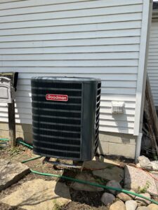 A new Goodman outdoor AC unit installed next to a house exterior with rocks and a garden hose by Buckeye Mechanical Construction in Columbus, OH.