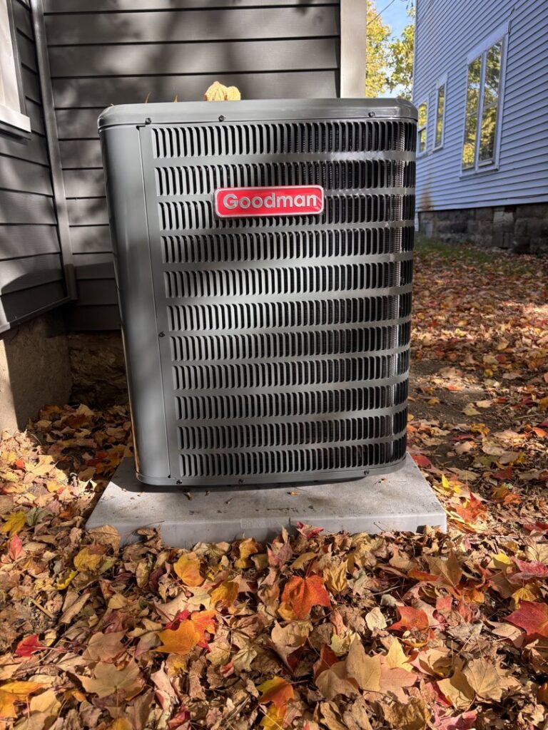 A new Goodman outdoor AC unit installed on a concrete pad, surrounded by autumn leaves, by Buckeye Mechanical Construction in Columbus, OH.