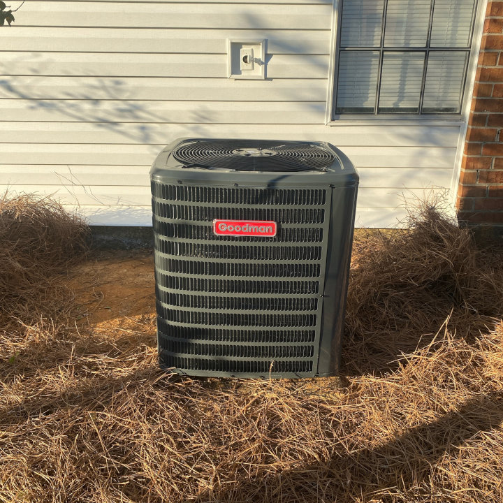 A newly installed Goodman outdoor HVAC condenser unit next to a residential building, installed by Eleven Heating and Cooling in Birmingham, AL.