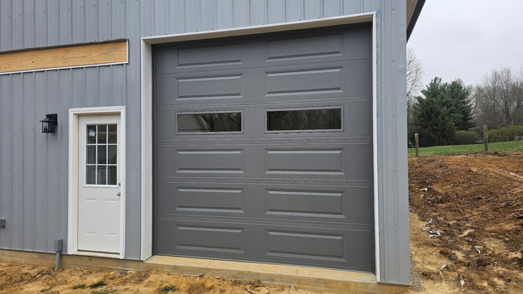 A newly installed gray garage door with windows on a building exterior by A+ Garage Door Repair in Evansville, IN.