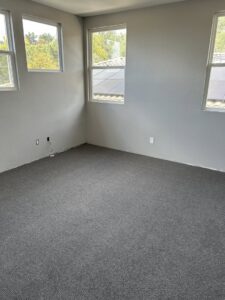 An empty bedroom showcasing a newly installed grey carpet by Floor & More in San Marcos, CA.