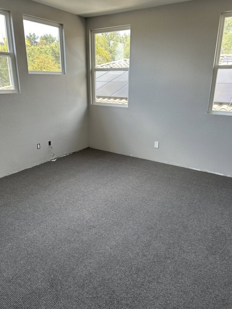 An empty bedroom showcasing a newly installed grey carpet by Floor & More in San Marcos, CA.