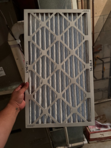 A hand holding a new HVAC air filter (14x24x1) ready for replacement, demonstrating a service by GUS' HVAC Services in Canton, GA.