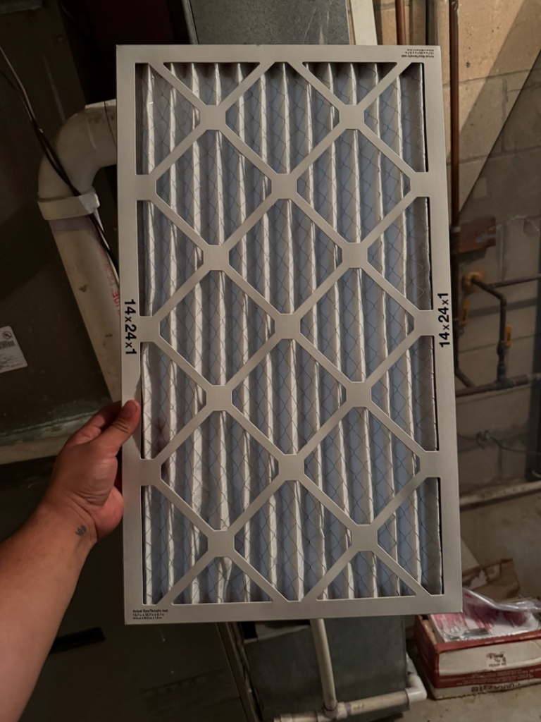 A hand holding a new HVAC air filter (14x24x1) ready for replacement, demonstrating a service by GUS' HVAC Services in Canton, GA.