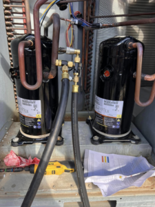 Two new HVAC compressors installed with refrigerant lines and service hoses by Mead Heating and Cooling in Kansas City, MO.