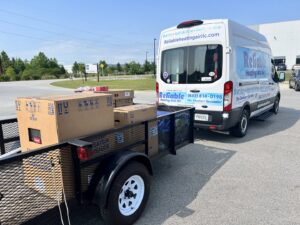 A Reliable Heating and Air LLC van with a trailer delivering new HVAC equipment for installation in Summerville, SC.