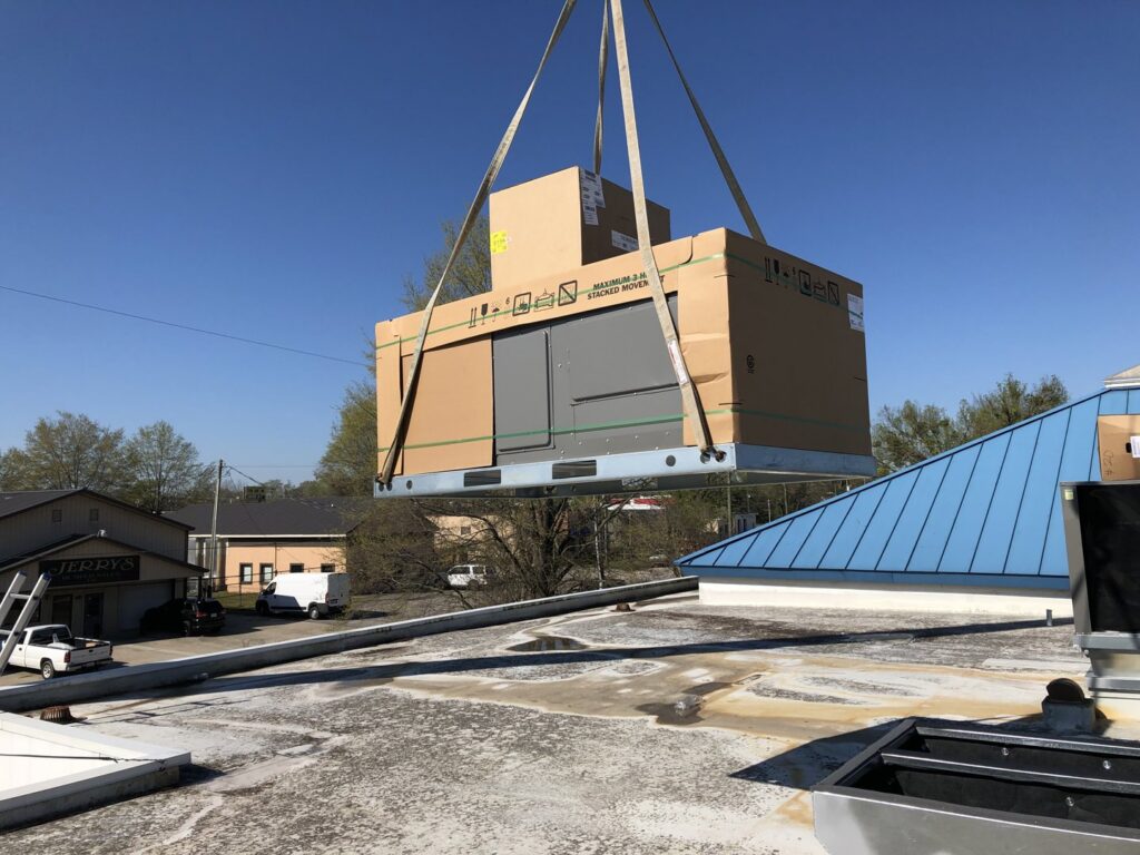 A new HVAC unit in packaging being lifted by a crane onto a commercial rooftop by Deon Arnold Heating & Air Conditioning in Fayetteville, NC