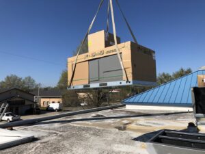 A new HVAC unit in packaging being lifted by a crane onto a commercial rooftop by Deon Arnold Heating & Air Conditioning in Fayetteville, NC