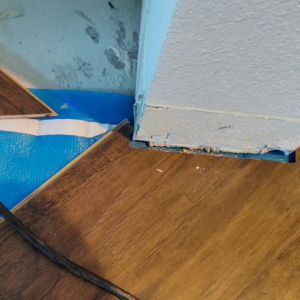 Close-up of new laminate flooring being installed around a corner with blue underlayment by Steam Vs. Soil Carpet Cleaning in San Diego, CA