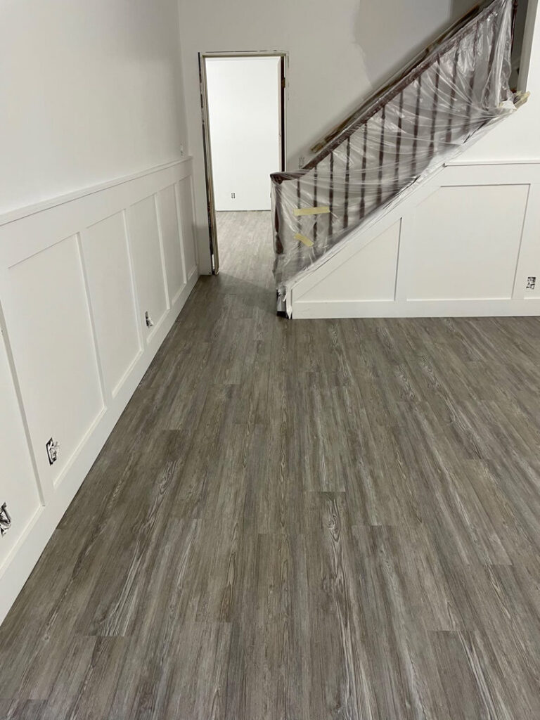 A newly installed laminate or vinyl plank flooring in a room with stairs covered for protection by Sy's Discount Carpets in Los Angeles, CA
