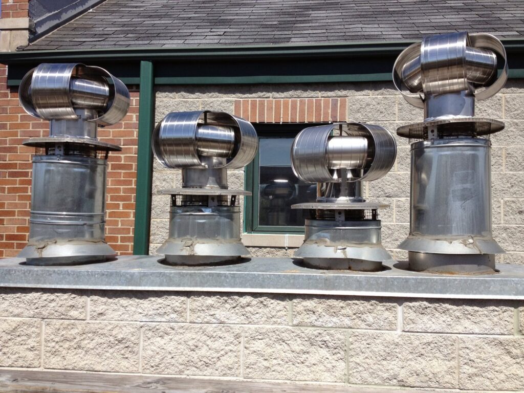 Four new metal chimney caps and vents installed on a rooftop by Chimney Usa Inc in Chicago, IL.