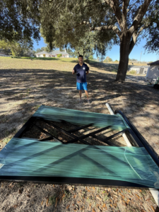 A new black metal gate, wrapped and ready for installation, on the ground by All With Us LLC in Green Cove Springs, FL.
