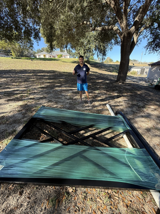 A new black metal gate, wrapped and ready for installation, on the ground by All With Us LLC in Green Cove Springs, FL.