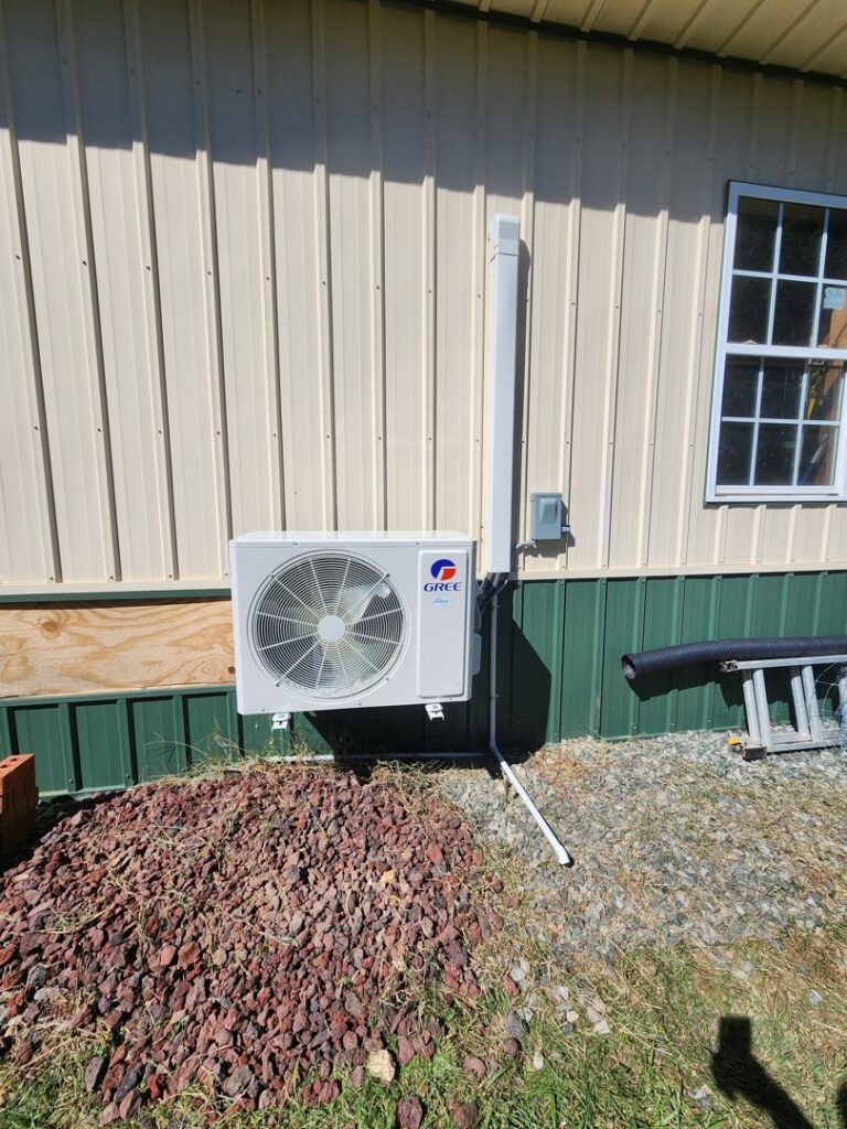 A new GREE mini-split outdoor unit installed on the side of a metal building by Sizemore Heating & Air, LLC in Chapel Hill, NC