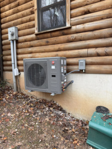 A newly installed Rheem outdoor HVAC unit on a log cabin, expertly placed by Dynamic Comfort Solutions in York, PA.