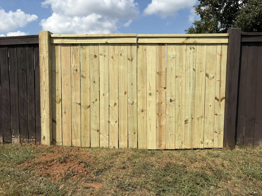 A newly installed single wooden gate or panel, light-colored, integrated into an existing dark fence by Myers & Dunlap Fence Repair in Greenville, SC.