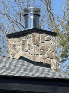 A newly installed stainless steel chimney cap on a stone chimney by Soot Busters in Birmingham, AL.