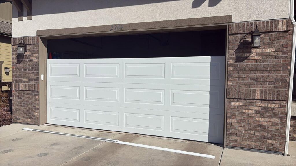 A new white panel garage door being installed or repaired at a residential property by Greeley garage door repair in Greeley, CO.