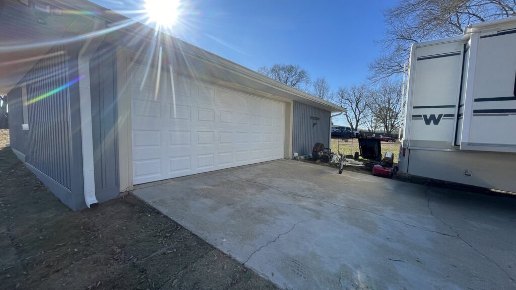 A new white garage door installed on a light blue sided garage by The Birmingham Man Garage Doors in Birmingham, AL.