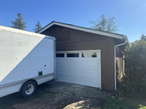 A newly installed white garage door with windows on a residential brown building by Reed's Garage Door Systems LLC in Sutherlin, OR.