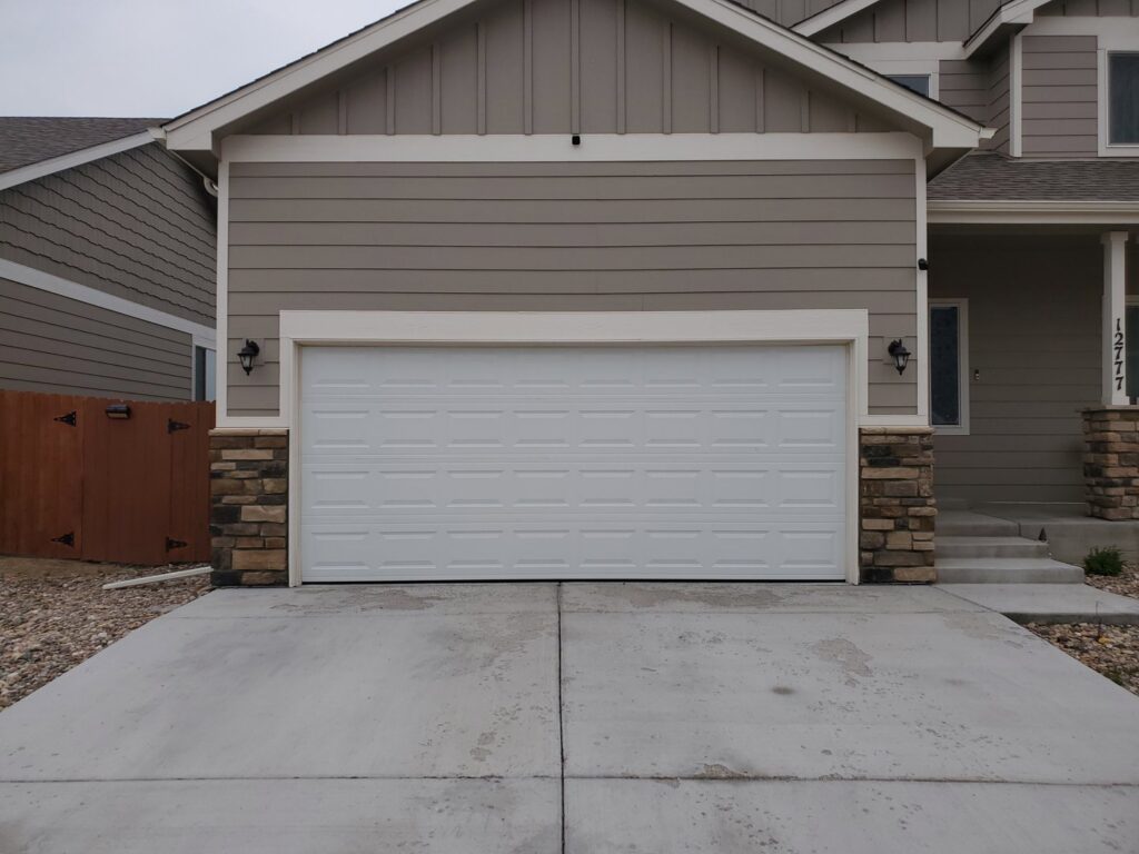 A newly installed white sectional garage door on a residential home by Black Forest Door Repair in Colorado Springs, CO.