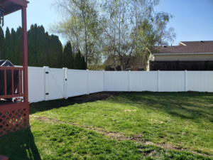 A newly installed white vinyl privacy fence with a gate in a backyard by Big Canyon Fencing in Lewiston, ID.