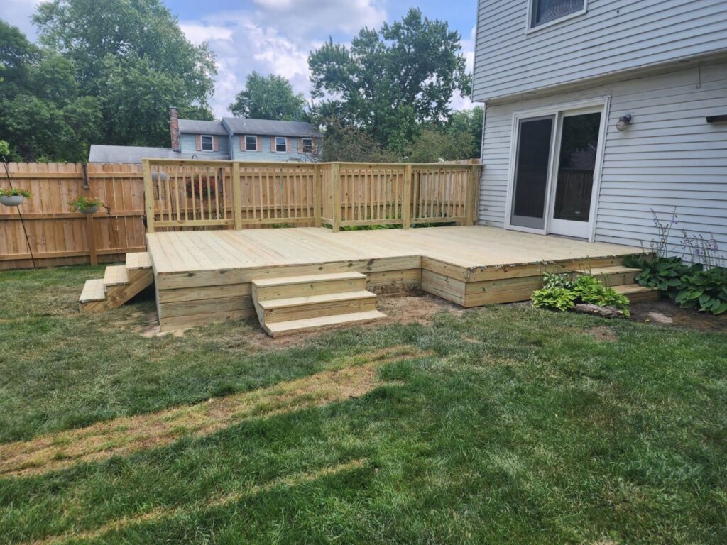 A new wood fence installed in a backyard with a deck by Barney's Landscaping in Dayton, OH.