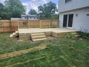 A new wood fence installed in a backyard with a deck by Barney's Landscaping in Dayton, OH.