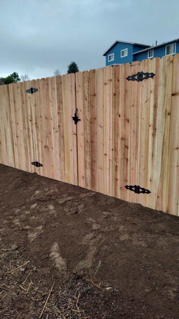 A newly installed wood fence featuring a double gate with decorative hinges, built by Good Neighbor Fencing, LLC in Colorado Springs, CO.