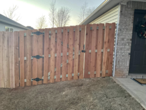 A newly installed wood fence gate with black hardware at the front of a house by Best Fences LLC in Springdale, AR.