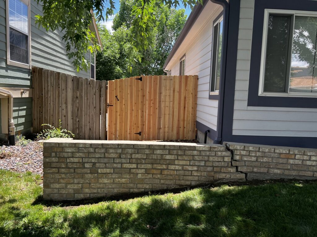 A newly installed wooden fence and gate on the side of a house by 2 Guys & A Girl Lawn Care in Thornton, CO.