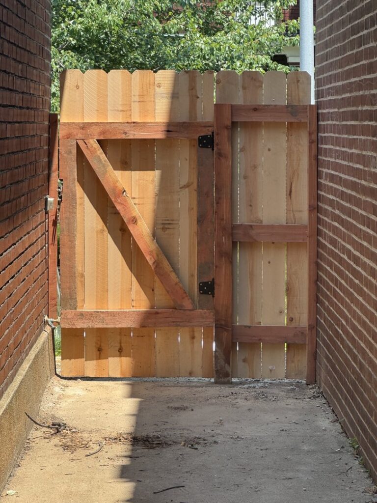 A newly installed custom wood fence gate between two brick walls by Exterior Experience LLC in St. Louis, MO.