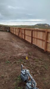 A newly installed wood fence with a gate, bordering a utility area, completed by Good Neighbor Fencing, LLC in Colorado Springs, CO.