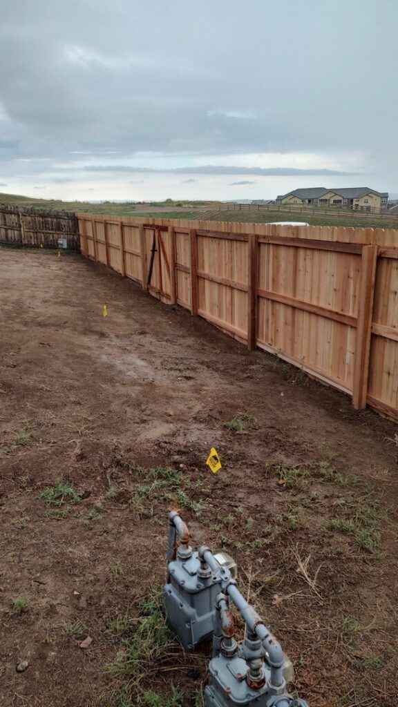 A newly installed wood fence with a gate, bordering a utility area, completed by Good Neighbor Fencing, LLC in Colorado Springs, CO.