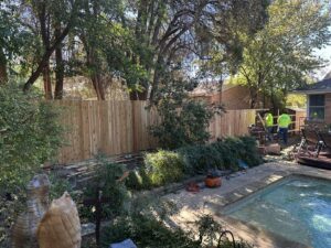 Workers installing a new natural wood fence in a backyard with a pool, provided by NTX-Exterior Services in Dallas, TX.