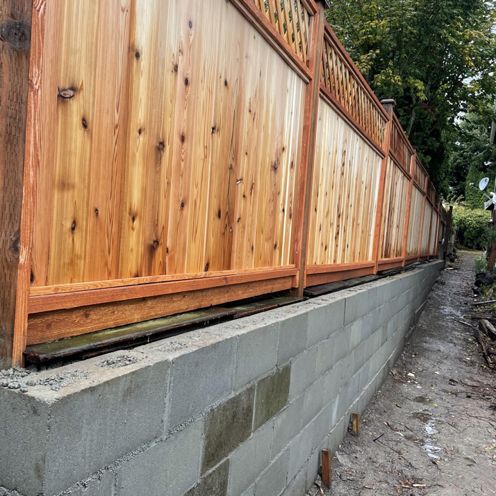 A newly installed wooden fence with a decorative lattice top built on a concrete block retaining wall by A.T service in Kent, WA.
