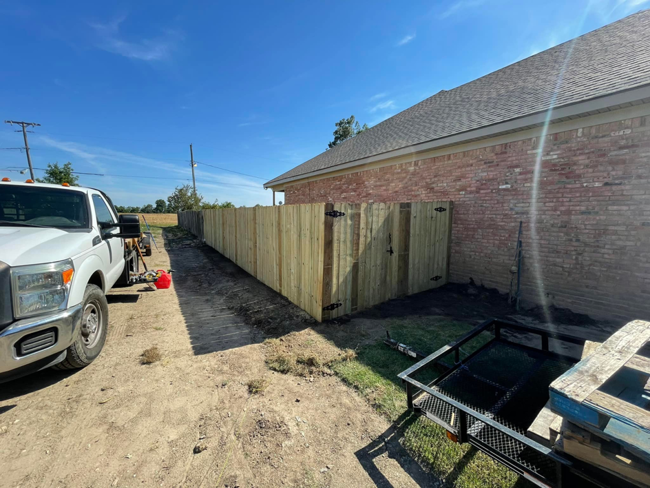A newly installed wood fence line with a gate next to a brick building by Swanson Fencing in Jonesboro, AR.