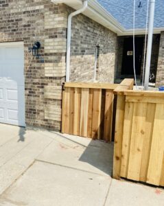 A newly installed wooden fence section next to a brick wall by 2 Guys & A Girl Lawn Care in Thornton, CO.