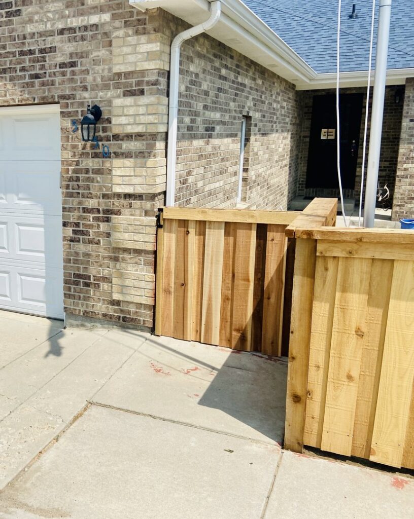 A newly installed wooden fence section next to a brick wall by 2 Guys & A Girl Lawn Care in Thornton, CO.