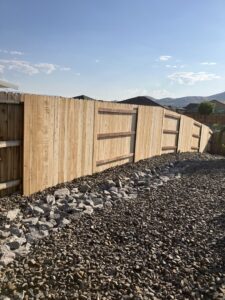 A newly installed wood privacy fence on a sloped backyard with a decorative rock bed by This And That Fence in Reno, NV.