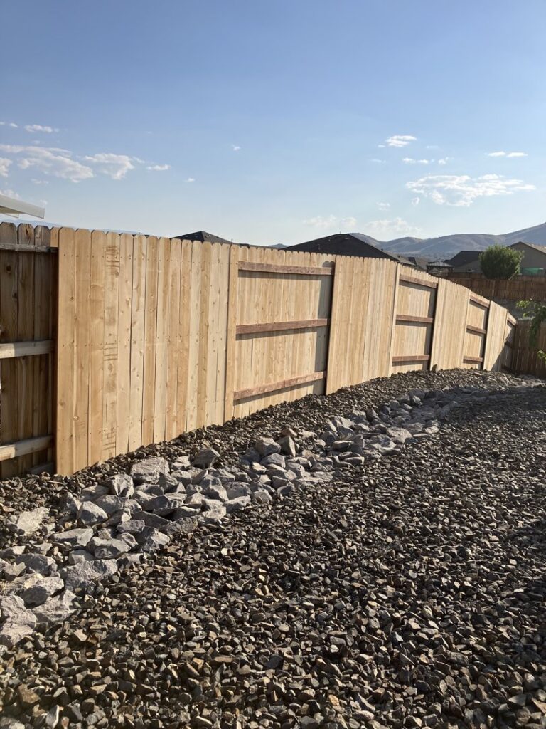 A newly installed wood privacy fence on a sloped backyard with a decorative rock bed by This And That Fence in Reno, NV.