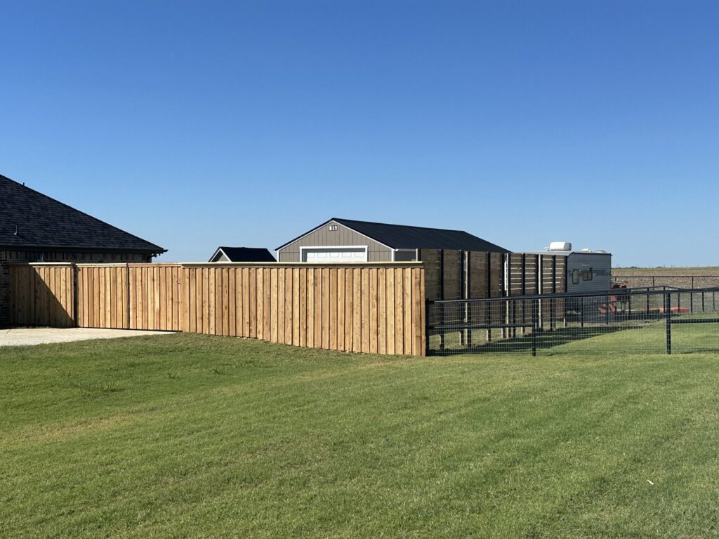 A newly installed natural wood fence transitioning into a black metal wire fence in a spacious backyard by NTX-Exterior Services in Dallas, TX.