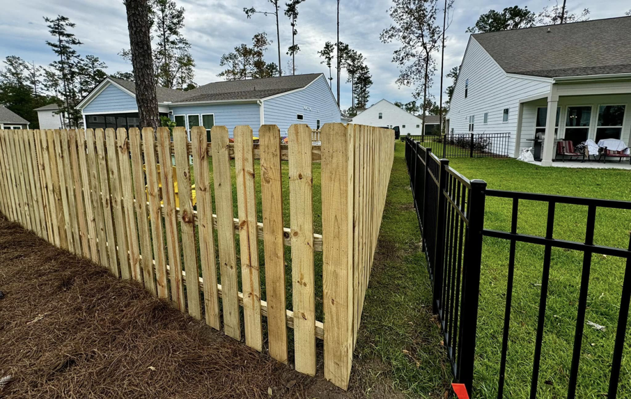 A new wooden picket fence alongside a black metal fence, showcasing work by Barwick Fence Company in Savannah, GA.