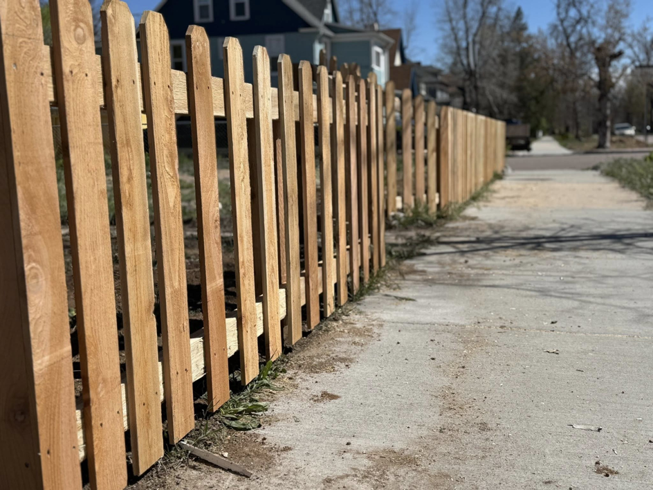 A newly installed wooden picket fence running alongside a sidewalk by Slater Fence Co in Houston, TX.