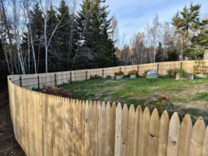 A newly installed wood picket fence curving around a residential backyard by Dirigo Fence Company in Augusta, ME.