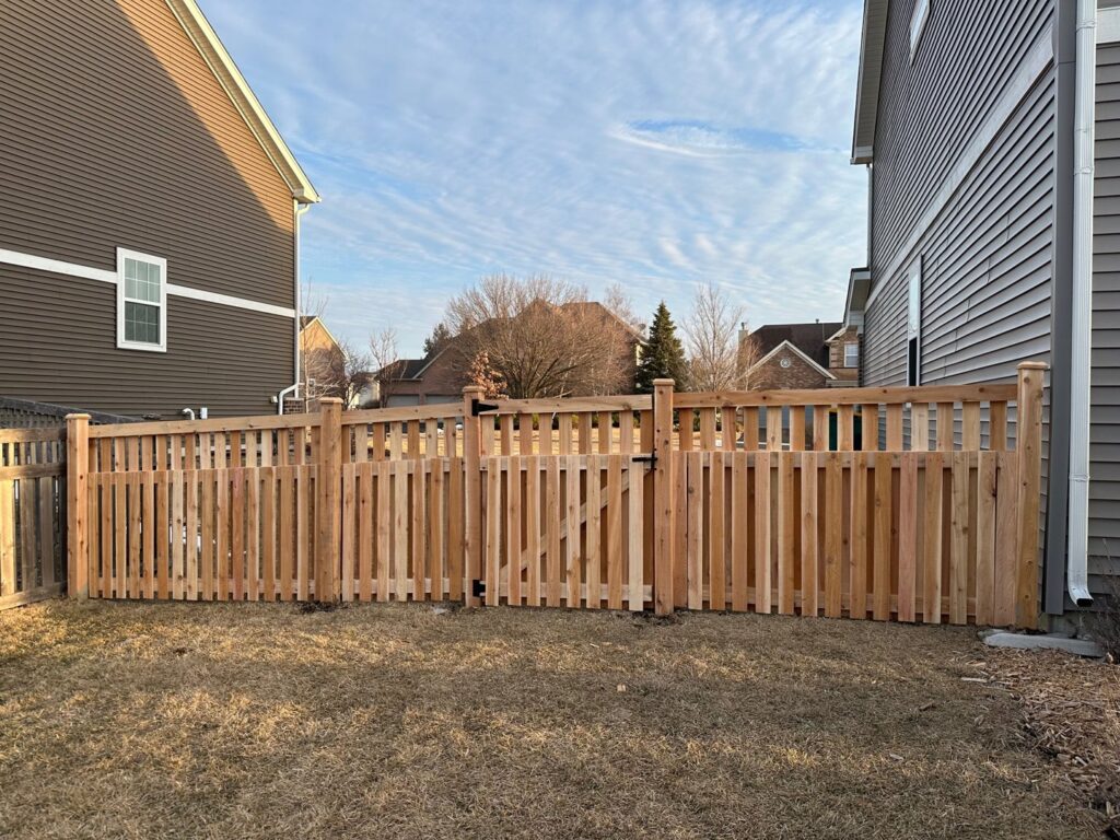 A newly installed wood picket fence with a gate between two residential houses by Cedar Mountain Fence Company in Plainfield, IL.