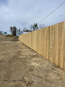 A newly installed tall wooden picket privacy fence running alongside a dirt area, completed by David Platania Fence in Derry, NH.