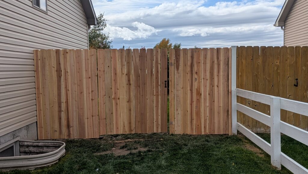 A newly installed wood privacy fence with a gate next to a house by 208 Fence and Gate in Idaho Falls, ID.