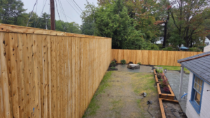 A newly installed tall wooden privacy fence in a residential backyard by Creative Fence in Casco, ME.