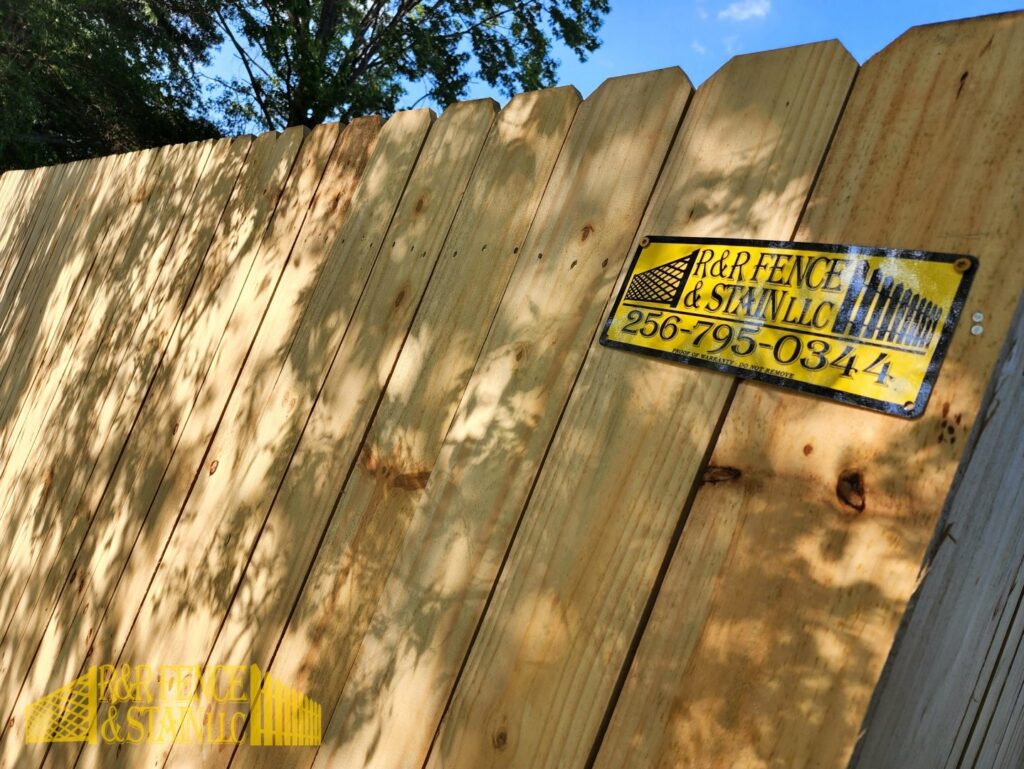 A close-up of a new wood privacy fence with the R&R Fence & Stain LLC business sign in Madison, AL.